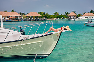 穿着红色比基尼的女人躺船弓上马尔代夫的暑